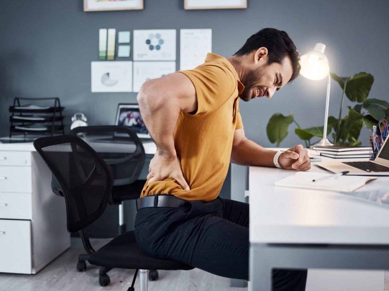 Business man, night and back pain or stress at office desk in a modern workplace . Asian male entrepreneur with injury and health, physical or burnout problem while tired and working late.